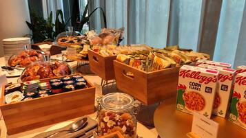 Una mesa de buffet con diversos alimentos, como pasteles, quesos y cereales.