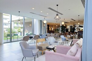 Una hall d'hotel moderna con diverse opzioni di seduta, ampie finestre e lampade dal design contemporaneo.