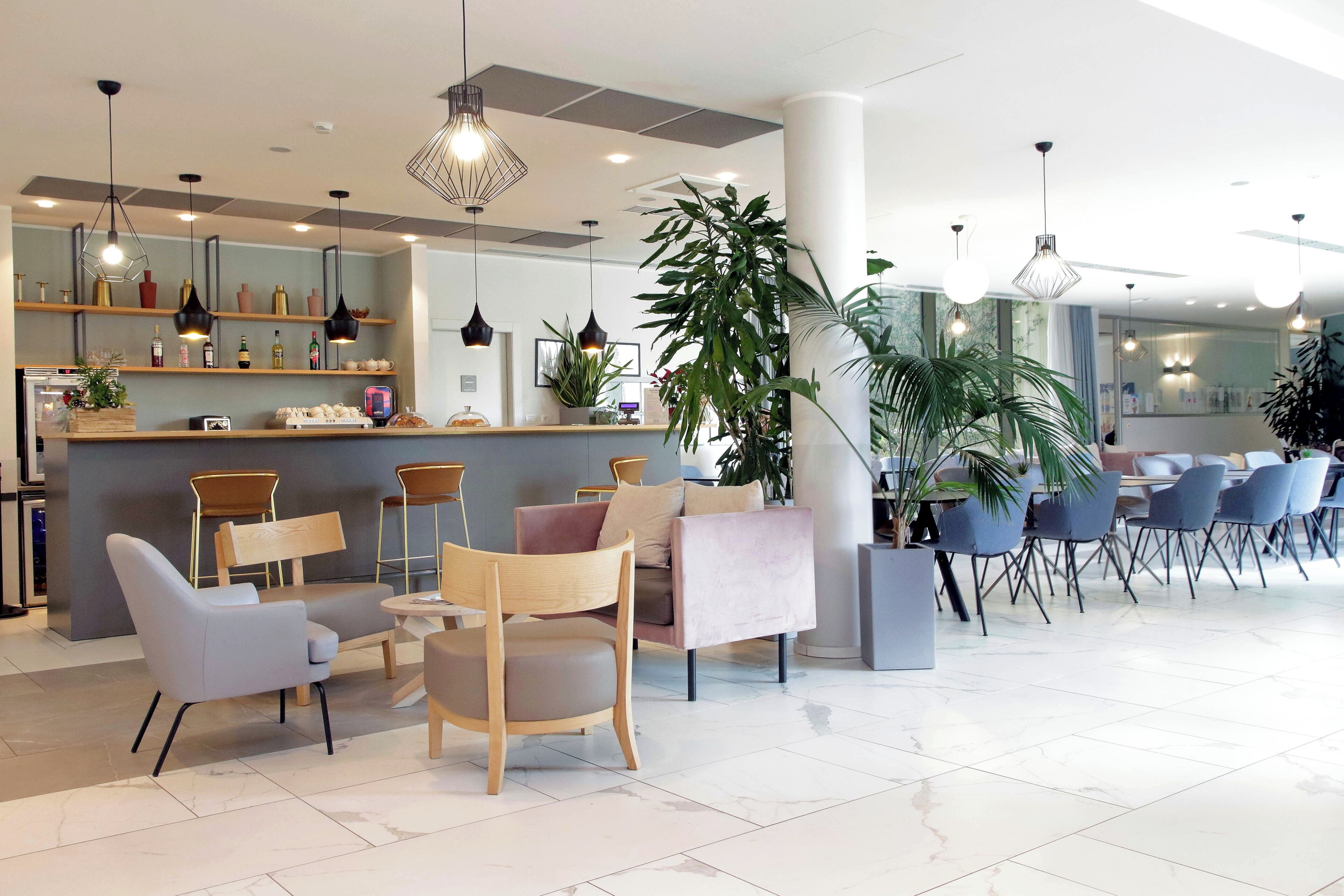 A modern hotel lobby with a reception desk, seating area, and potted plants.