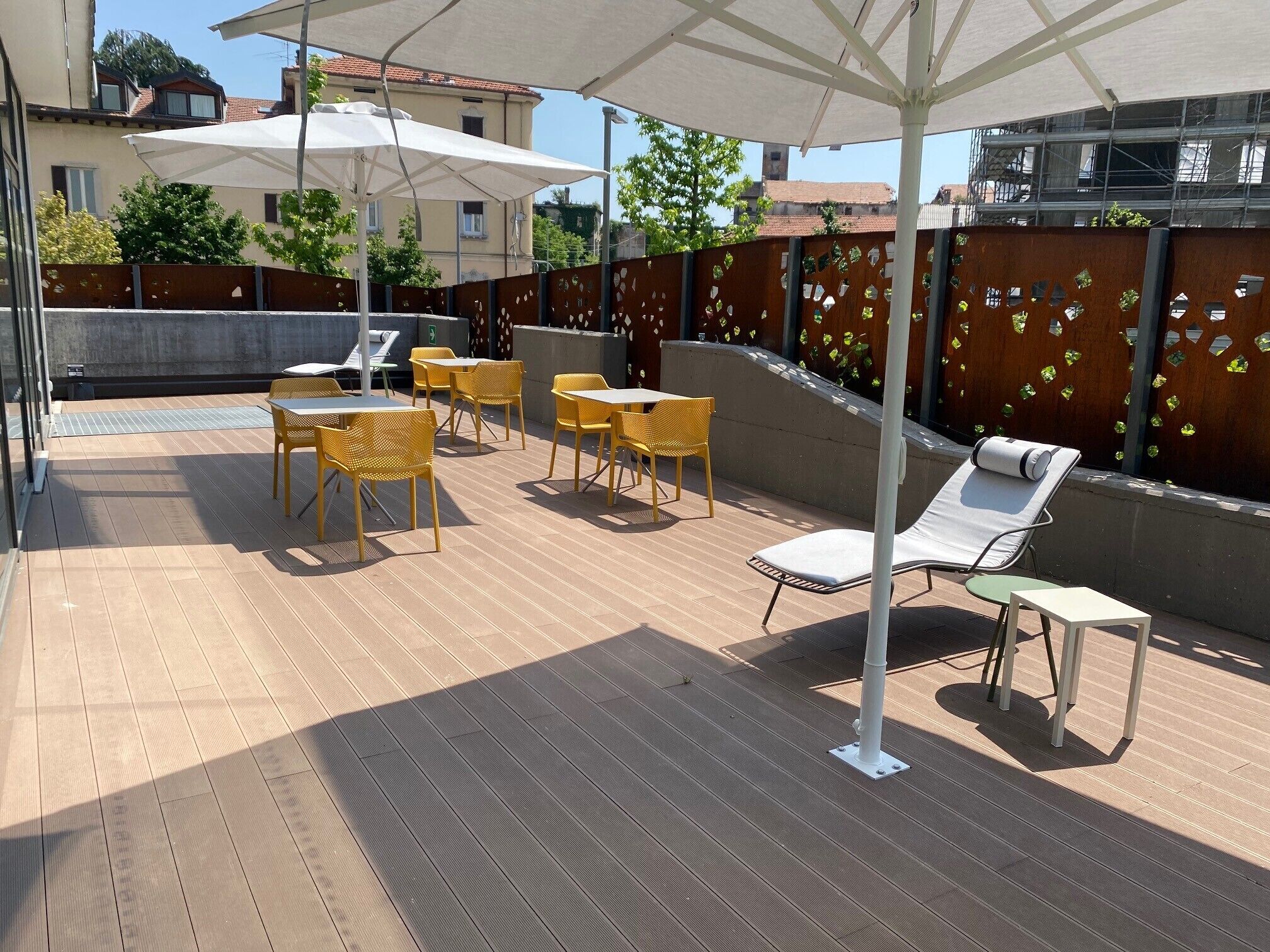 Un patio al aire libre con sillas y mesas amarillas, una tumbona y sombrillas que dan sombra.