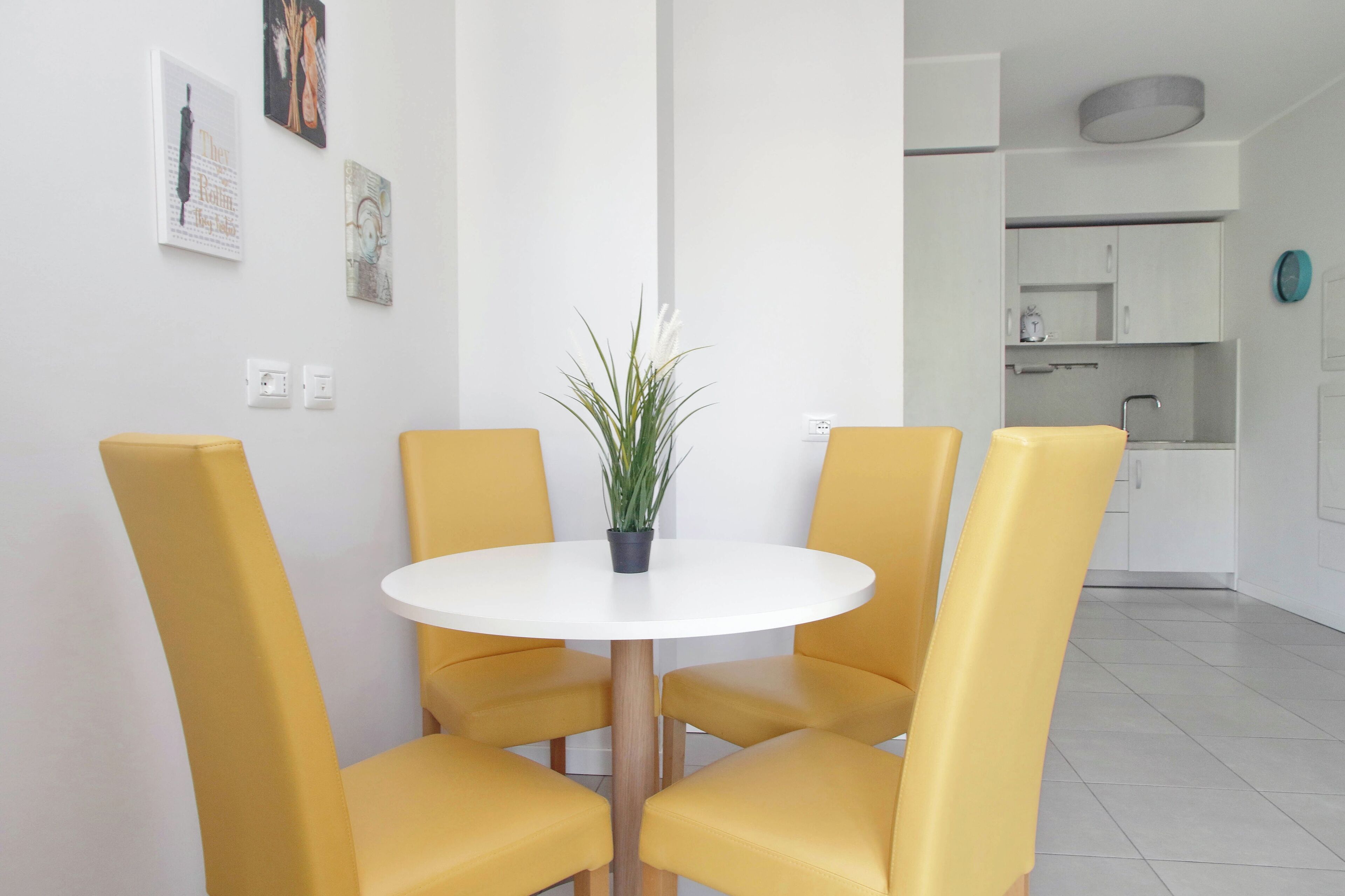 Un comedor moderno con una mesa redonda blanca, sillas amarillas y una planta en maceta.