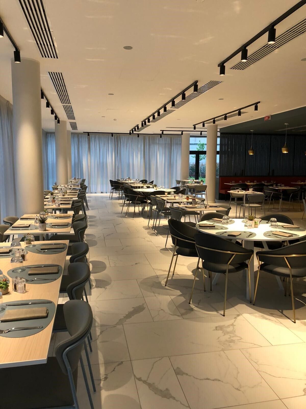 Un espace de restauration moderne, doté de longues tables et de chaises, de grandes fenêtres et d’un aménagement épuré et minimaliste.