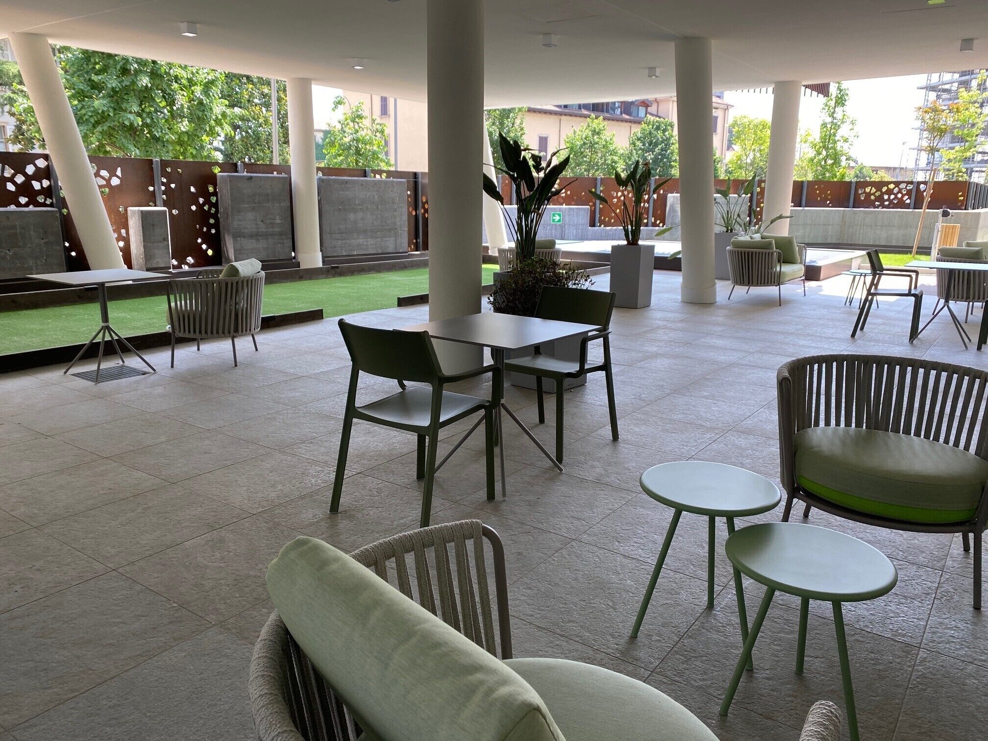 An outdoor seating area with tables and chairs, a grassy patch, and potted plants.