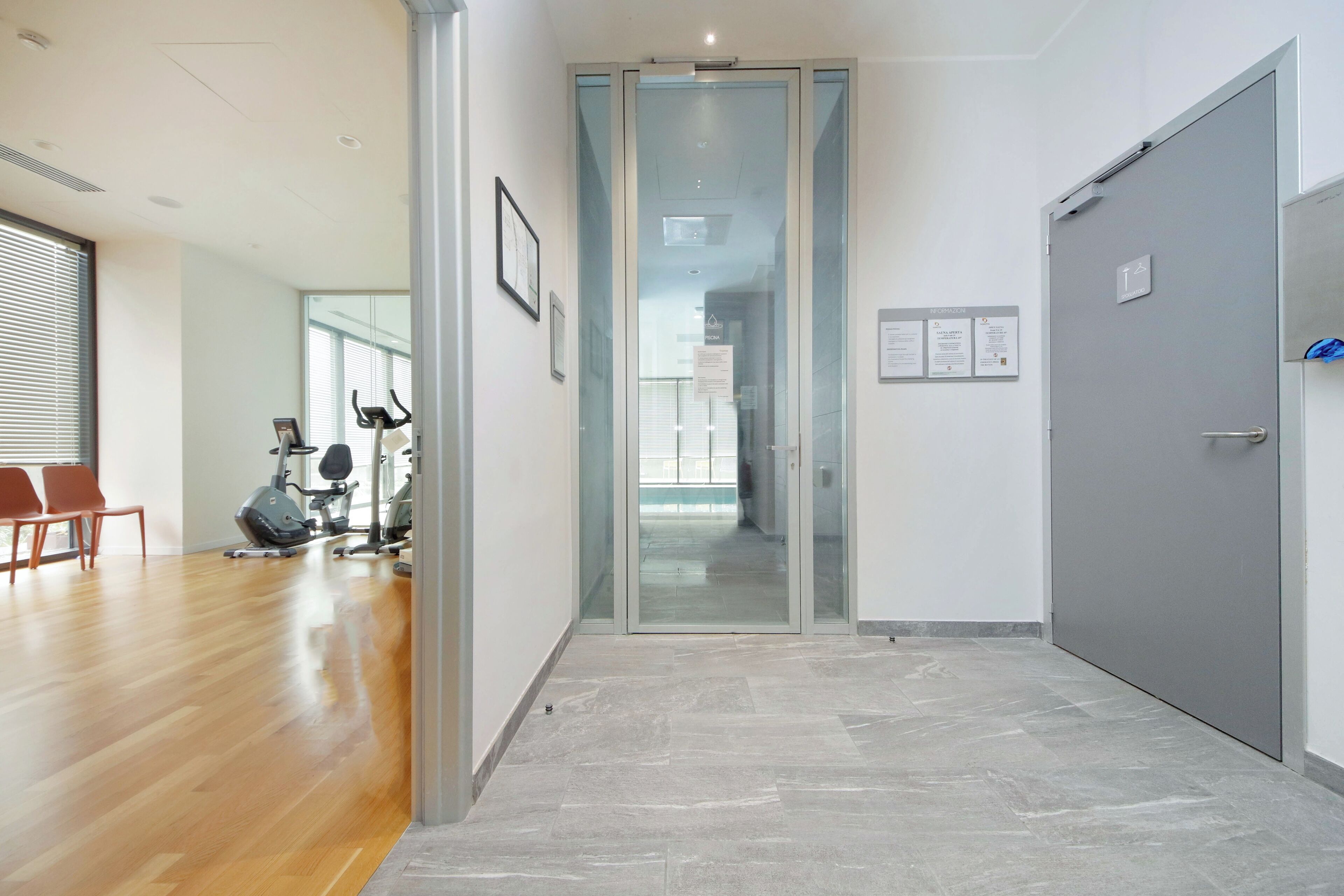 A hallway with a wooden floor, a glass door, and a grey door.