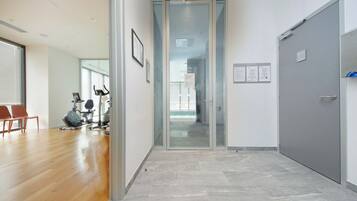 A hallway with a wooden floor, a glass door, and a grey door.
