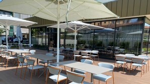 An outdoor café with tables and chairs, large umbrellas, and a view of the street. -  Quarto Verde Apartments (Bergamo)