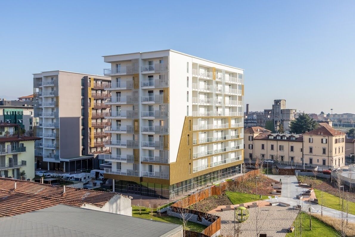A modern multi-story residential building with balconies, a rooftop terrace, and a parking area.