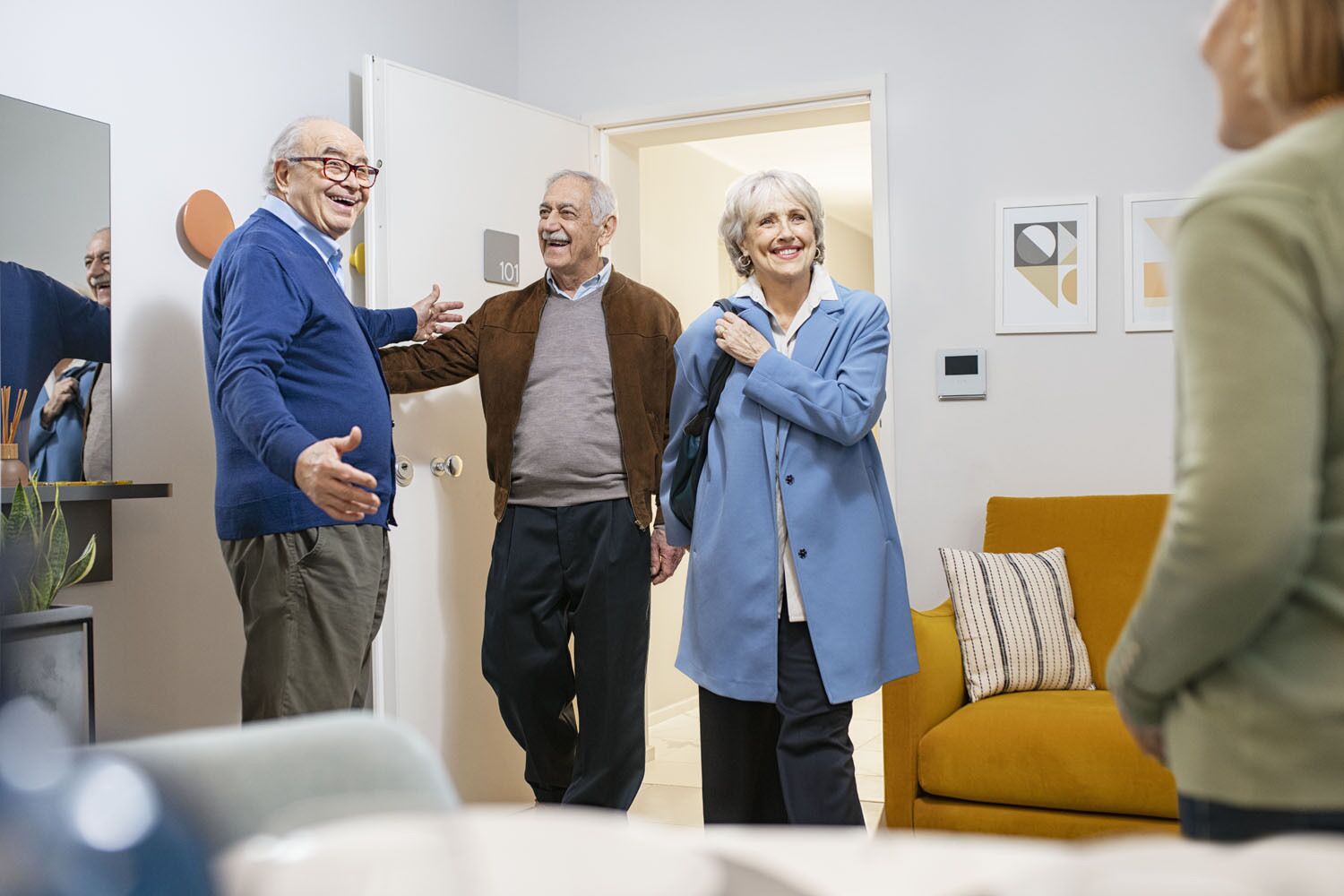 A group of people in a room with a sofa, a door, and a wall-mounted thermostat.