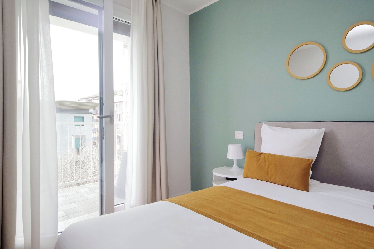 A hotel room with a bed, a nightstand, a lamp, and a view through a sliding door.