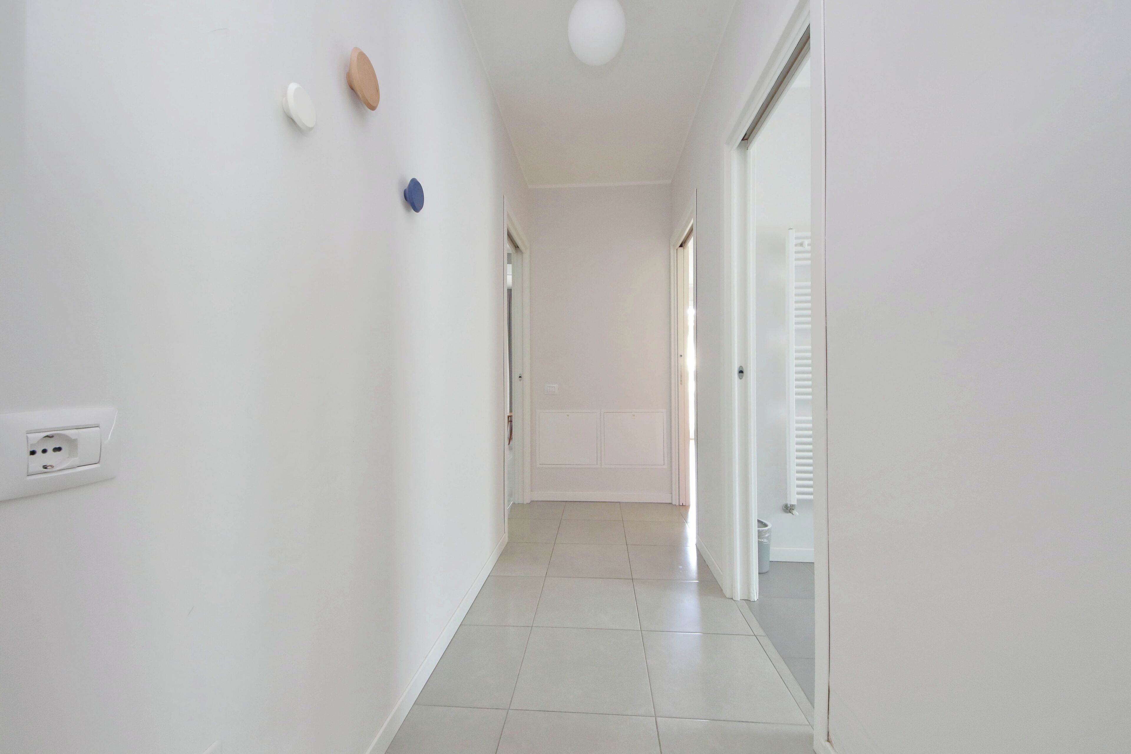 A hallway with white walls, a tiled floor, a ceiling light, and a door with a white shutter.