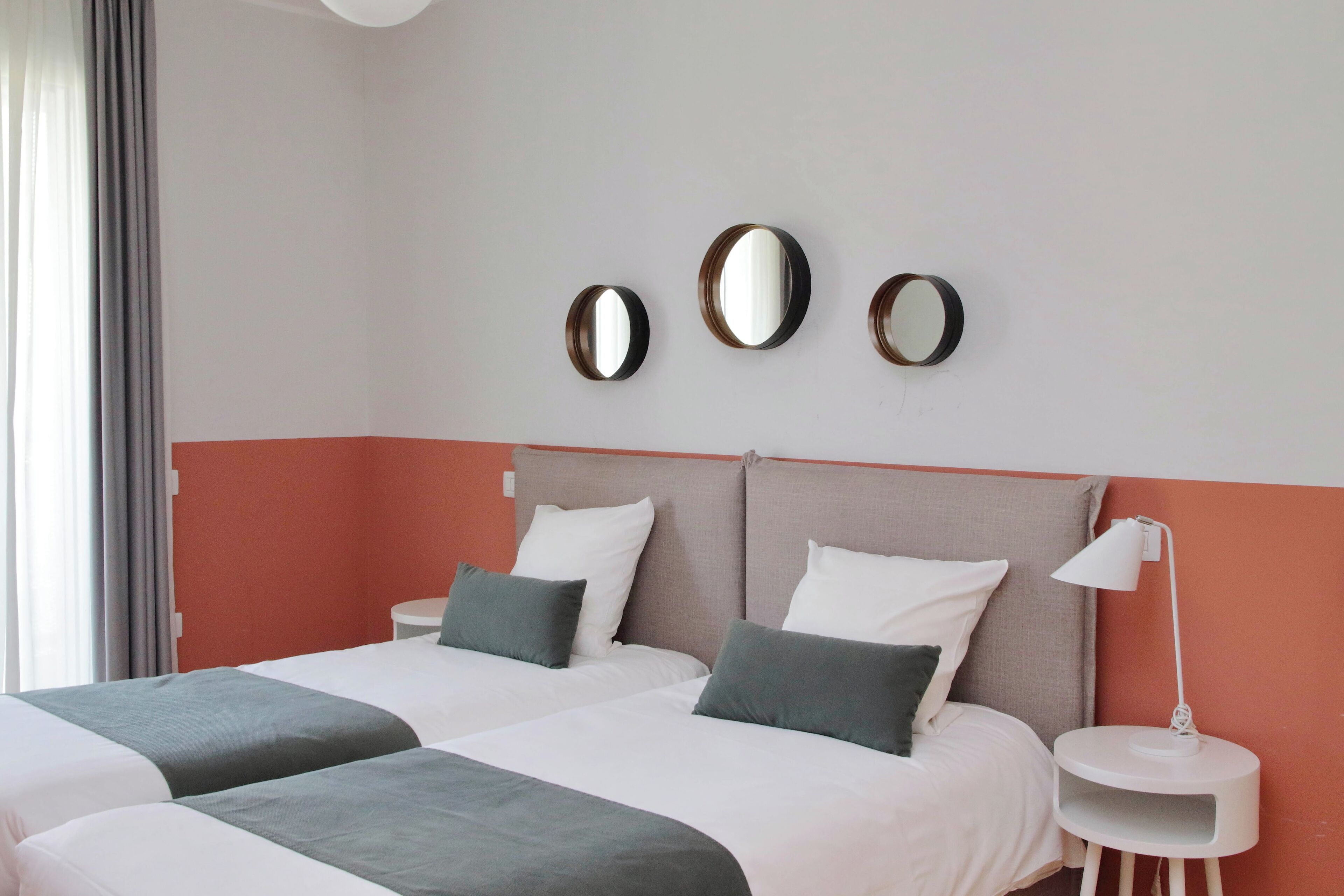 Ein Hotelzimmer mit zwei Betten, einem Nachttisch, einer Lampe und drei Wandspiegeln.