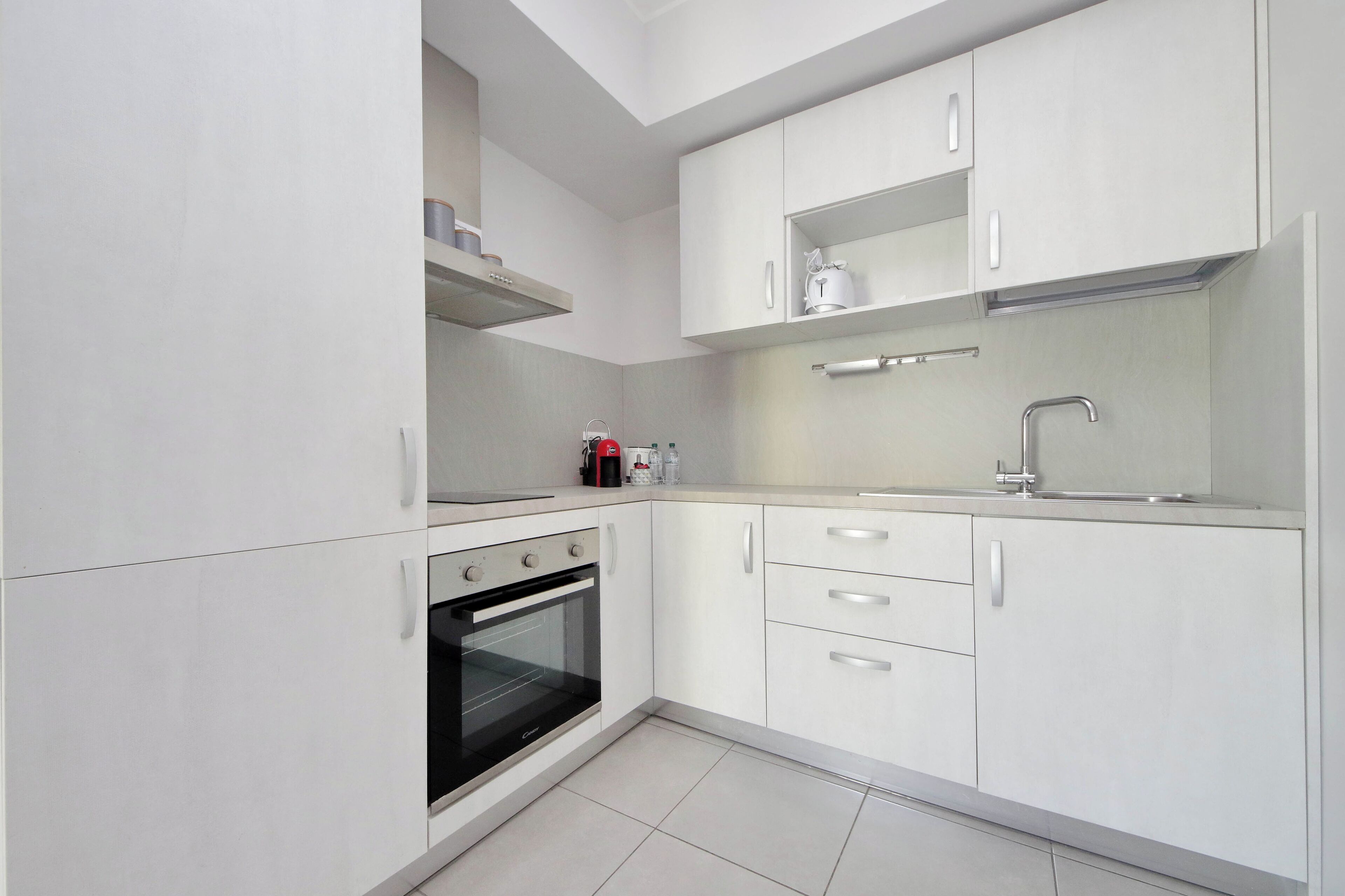 Een moderne keuken met witte kastjes, een inbouwoven, een spoelbak en een aanrecht met een waterkoker.
