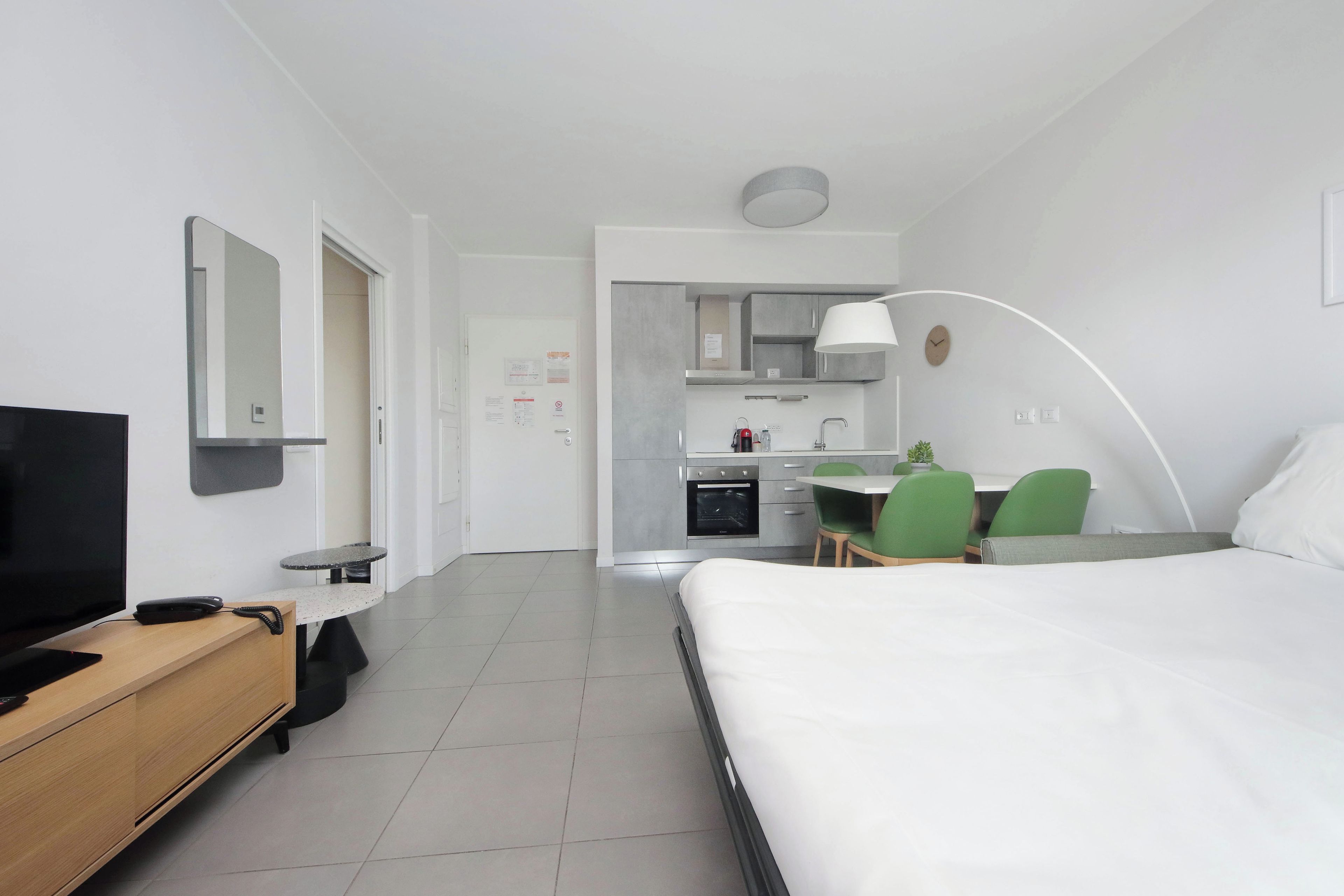 A hotel room with a bed, a desk, a TV, a chair, and a kitchenette.