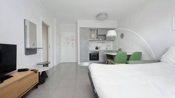 A hotel room with a bed, a desk, a TV, a chair, and a kitchenette.