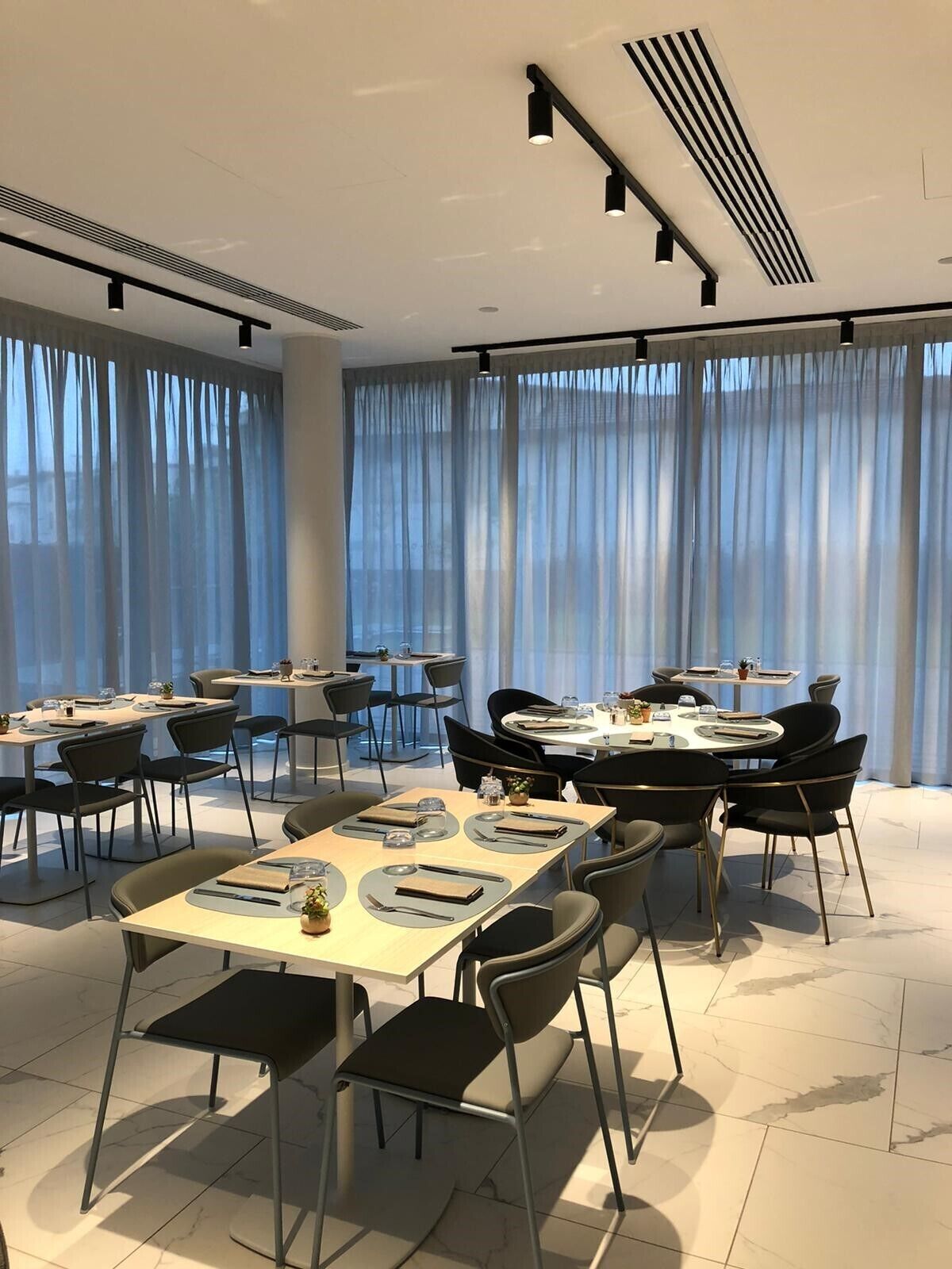 A modern conference room with round tables, black chairs, and a large window with sheer curtains.