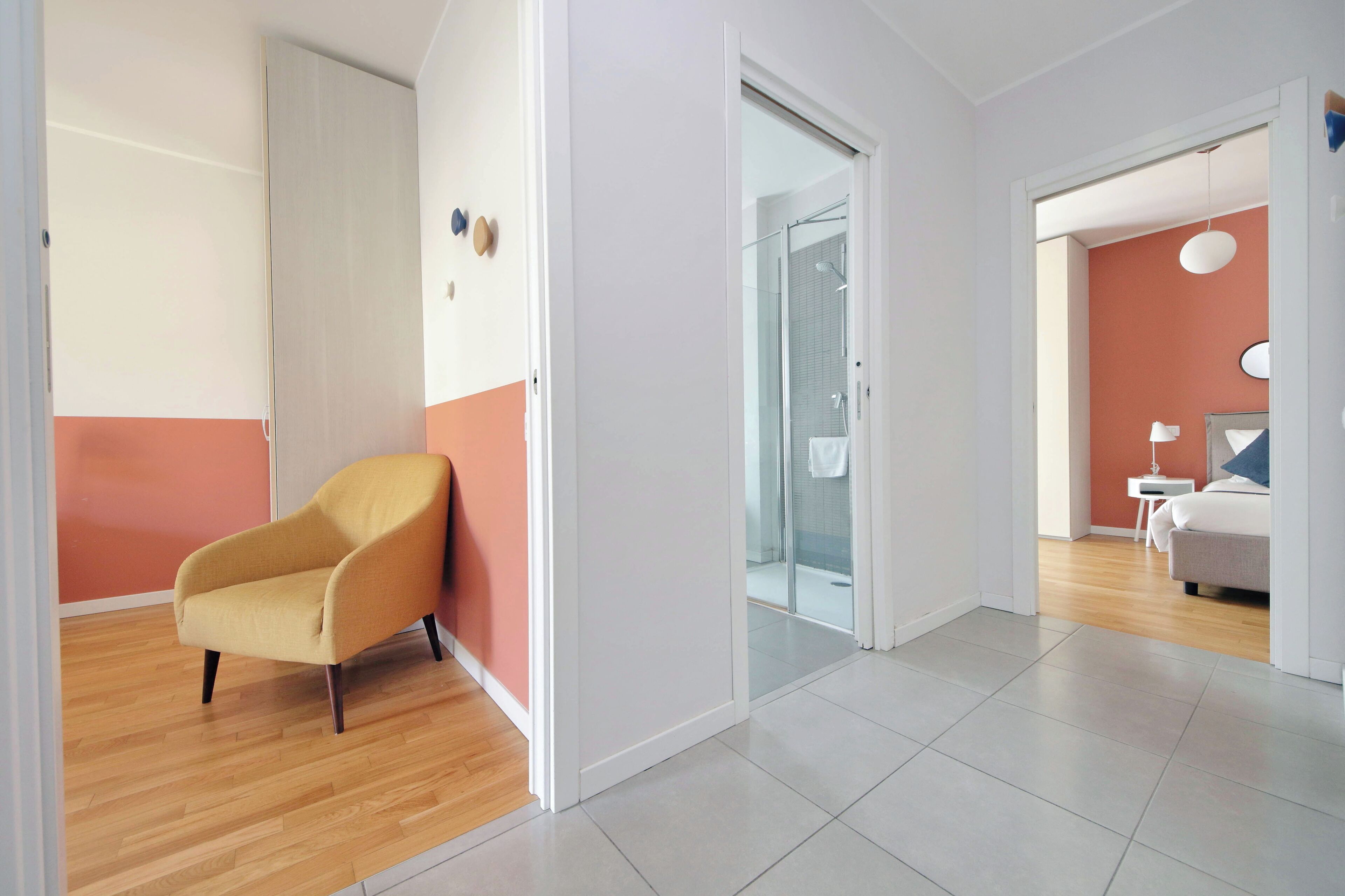 A modern apartment with a wooden floor, a yellow armchair, a glass shower, and a white bed.