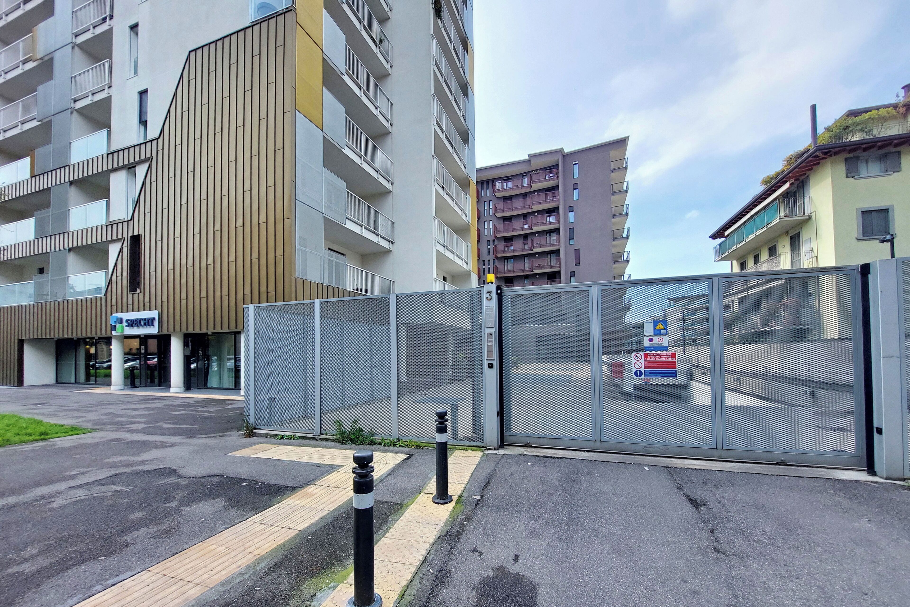 A gated entrance to a building with a modern design, a visible sign for a business, and a clear sky.