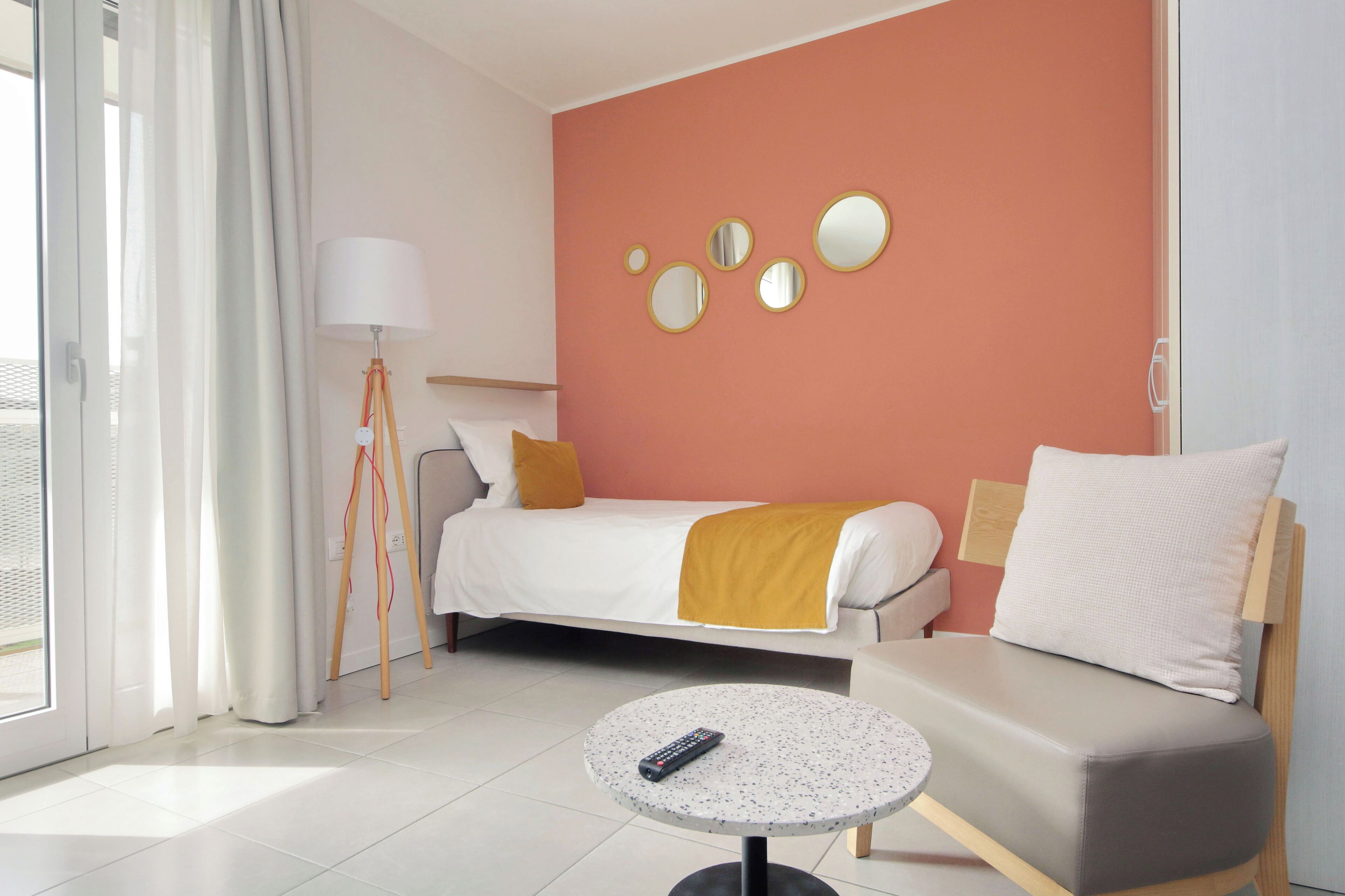 A hotel room with a bed, a sofa, a lamp, a round table, and wall-mounted mirrors.