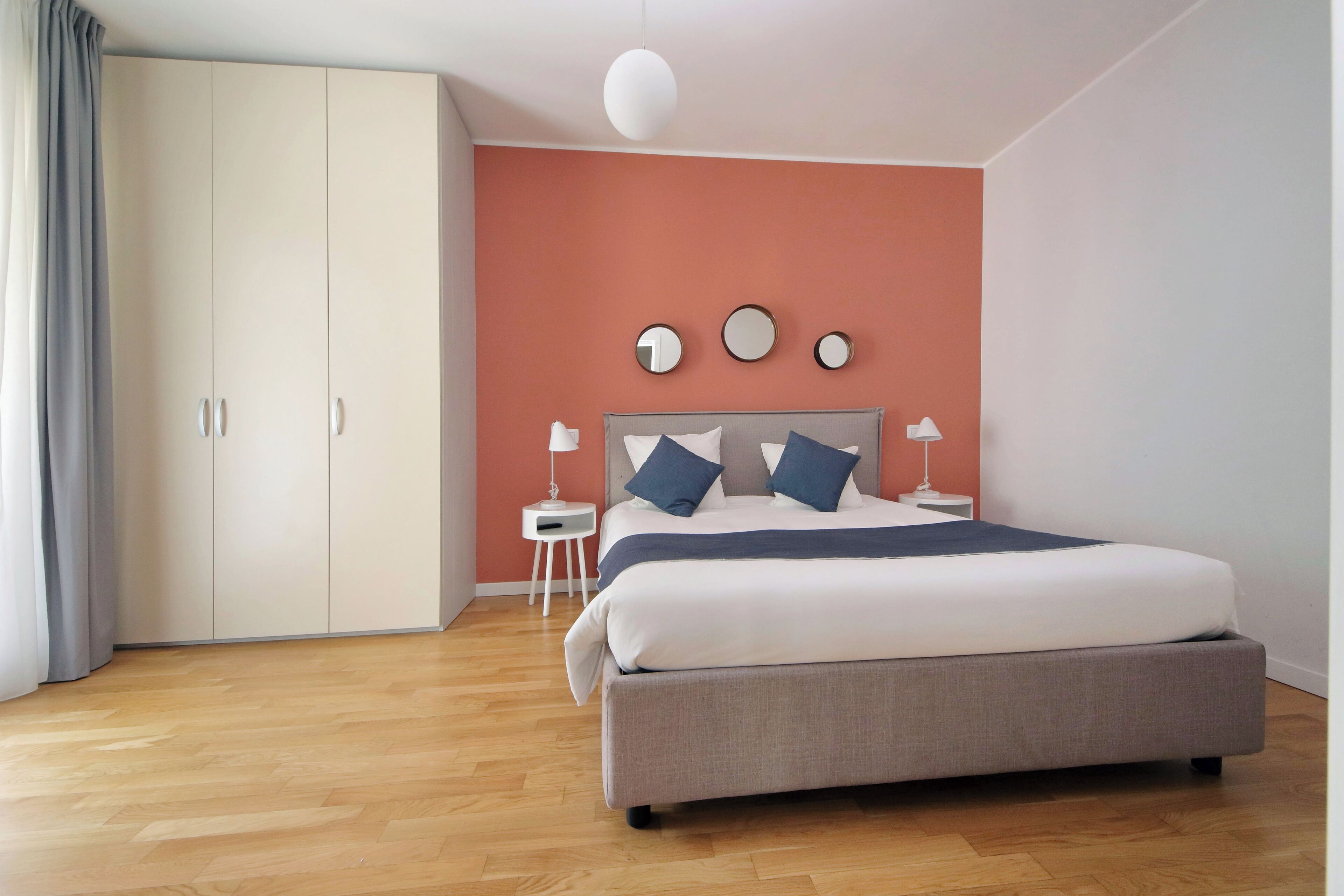 A bedroom with a bed, a wardrobe, a nightstand, and a wall-mounted mirror.