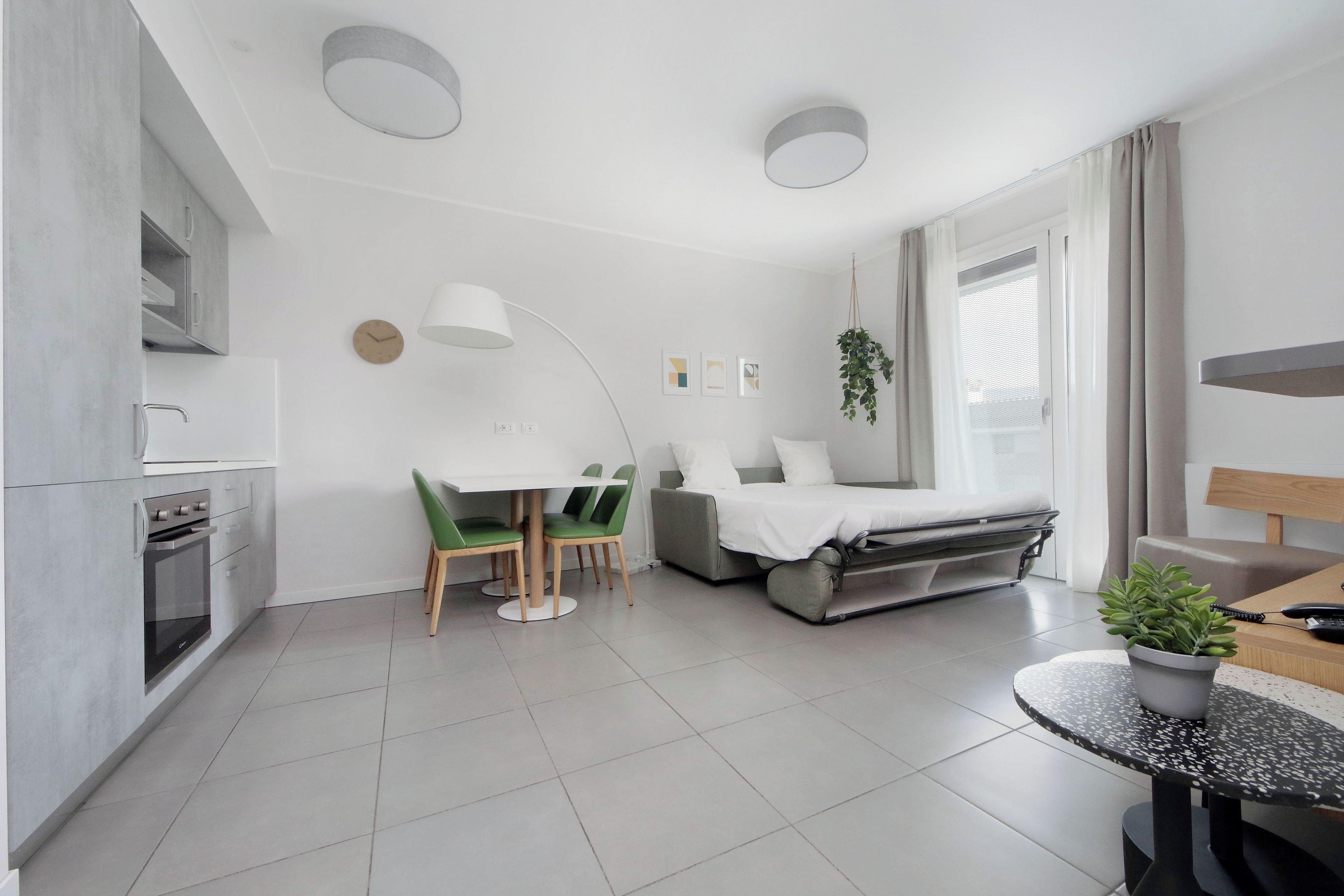 Een moderne, minimalistische woonruimte met een kitchenette, een eethoek, een slaapbank en een bijzettafeltje met een plant.