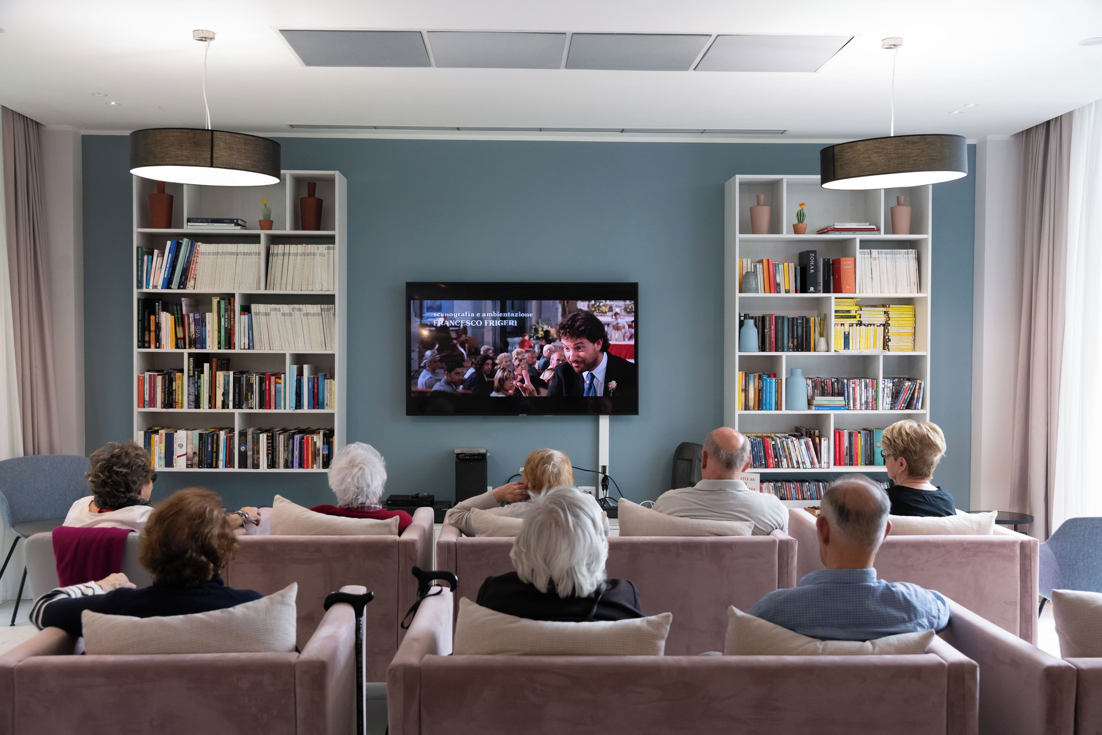 Ein modernes Wohnzimmer mit einem an der Wand befestigten Flachbildfernseher, umgeben von Bücherregalen voller Bücher.