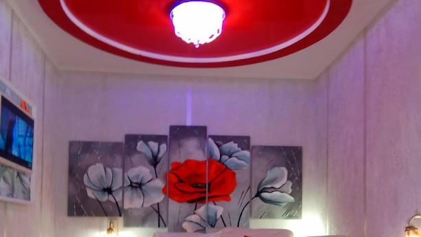 A bedroom with a red and white color scheme, a round ceiling light, and a large floral painting on the wall. - Shellman (Odesa)