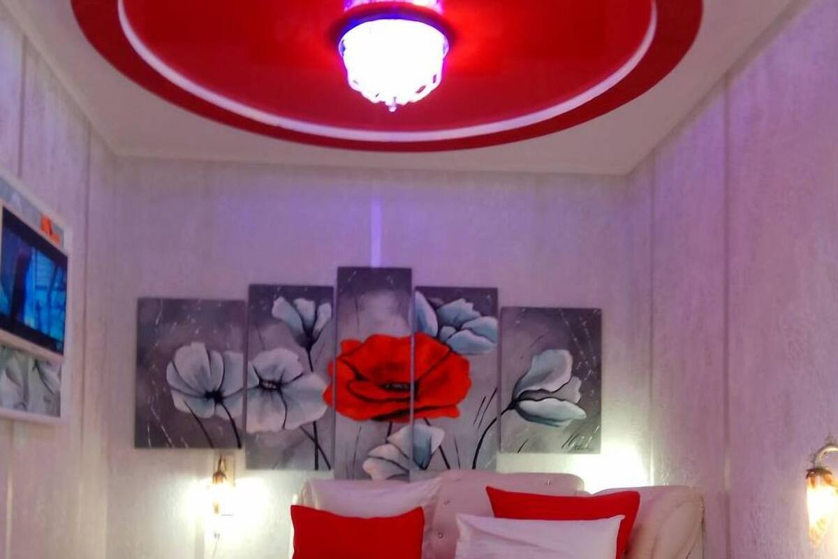 A bedroom with a red and white color scheme, a round ceiling light, and a large floral painting on the wall.