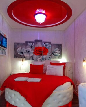 Un dormitorio con una decoración en rojo y blanco, una lámpara de techo redonda y un cuadro grande con motivos florales en la pared.