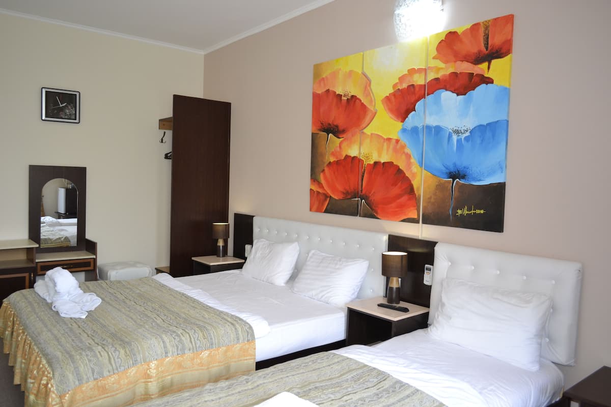 A hotel room with two beds, a large painting of flowers on the wall, a clock, and a mirror.