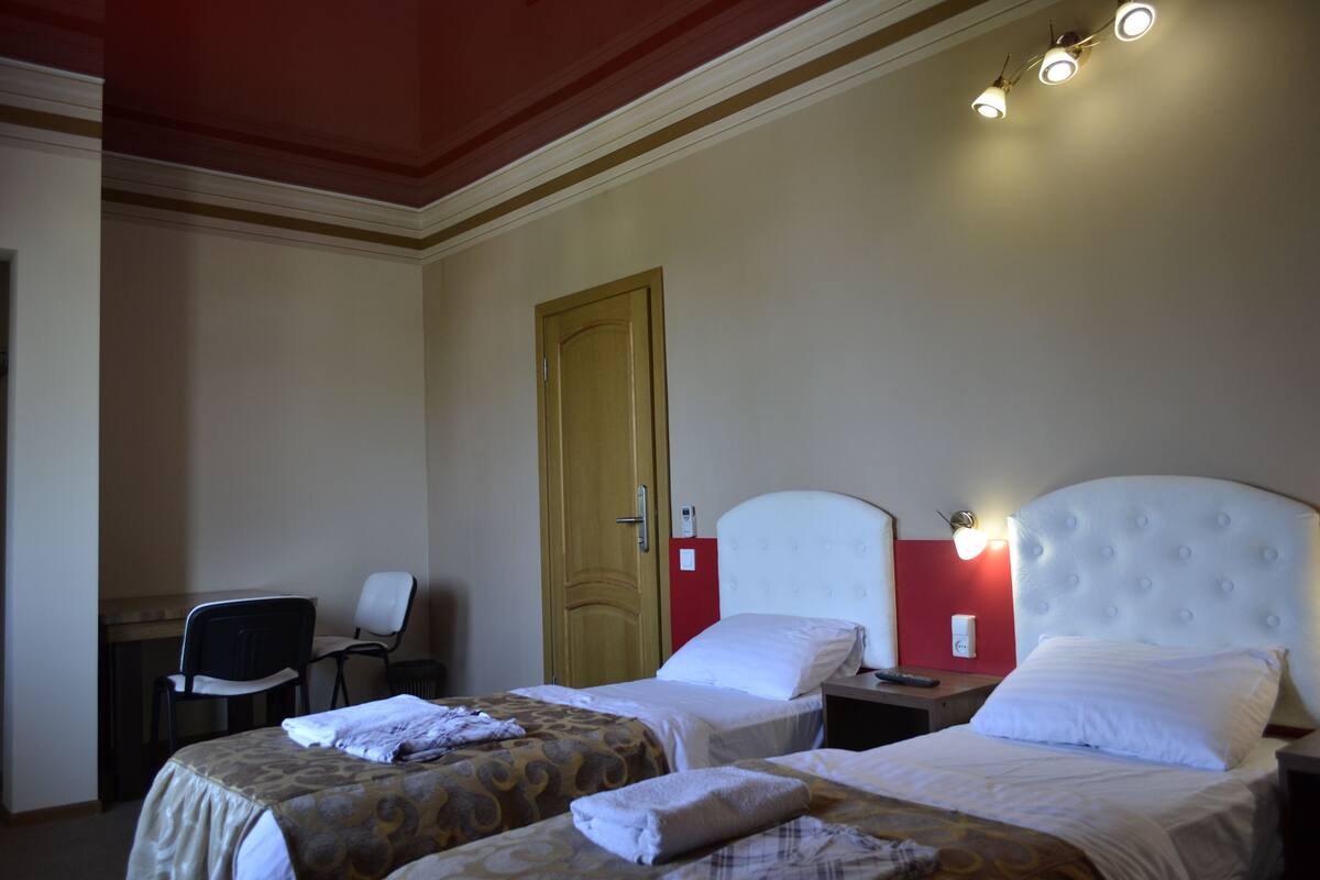 A hotel room with two beds, a desk, a chair, and a door.