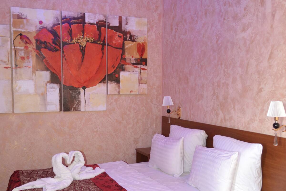 A hotel room with a large bed, a wooden headboard, a wall-mounted painting, and a nightstand with a lamp.