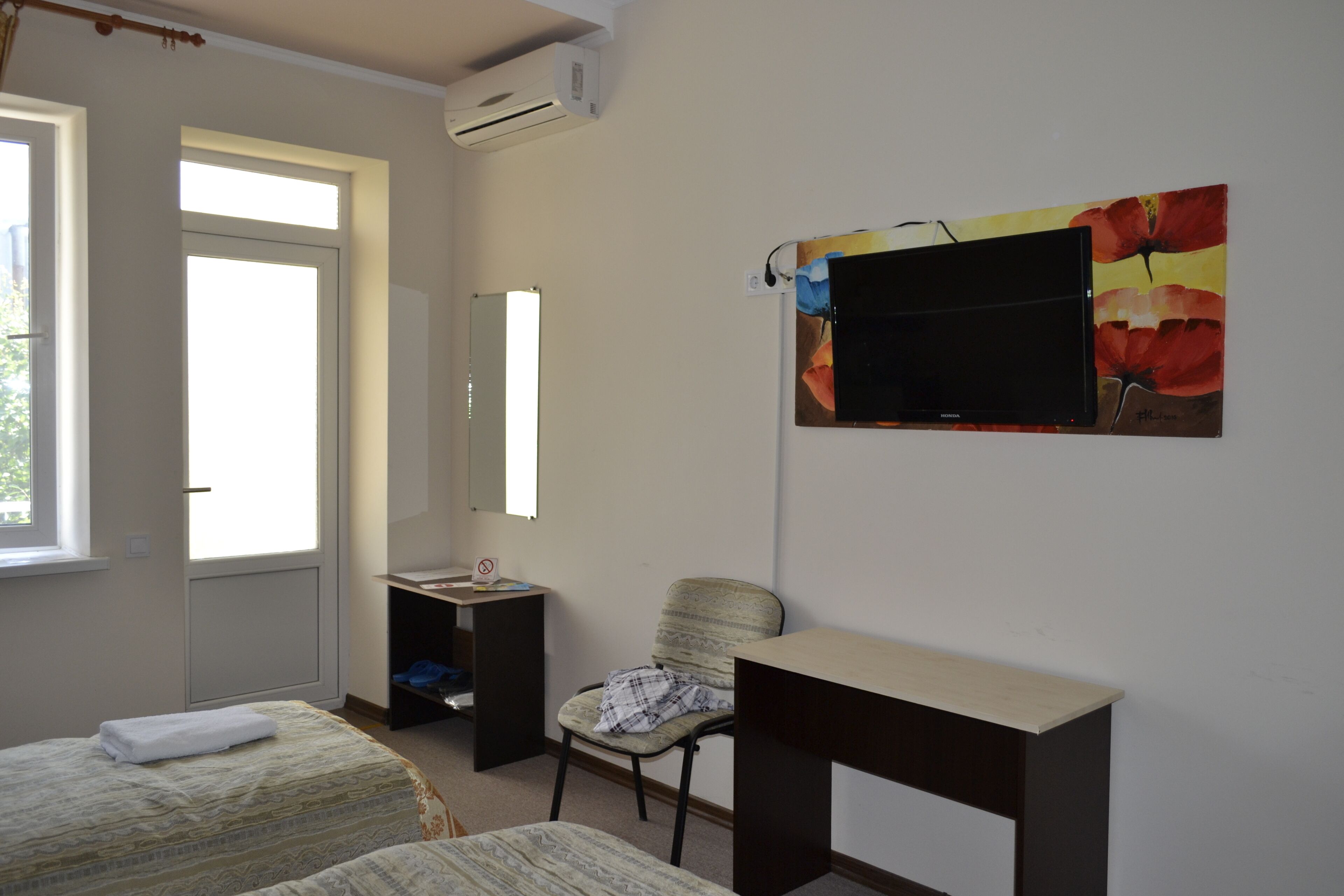 Une chambre d’hôtel avec deux lits, un bureau, une chaise, une télévision et une fenêtre.