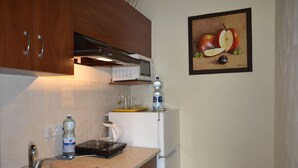 A kitchen with a sink, countertop, and a microwave. There is a water bottle, a kettle, and a framed picture of fruit on the wall. - Shellman (Odesa)