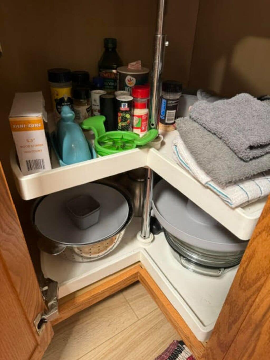 Une cuisine avec une étagère d’angle où sont rangés divers ustensiles, notamment un égouttoir vert, une boîte de savon liquide et une pile de serviettes.
