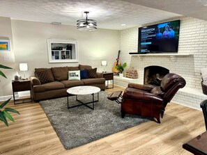 A living room with a fireplace, a television mounted above it, a sofa, a coffee table, and a leather armchair. - Private 1BR Suite w/ Own Entry · Walk to GMU (Fairfax)