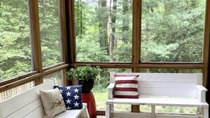 A covered porch with two white benches, one with a star-patterned pillow and the other with a red and white pillow.