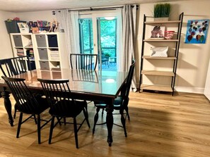 A dining area with a glass-top table and chairs, a bookshelf, and a view through a glass door to an outdoor deck. - Private 1BR Suite w/ Own Entry · Walk to GMU (Fairfax)