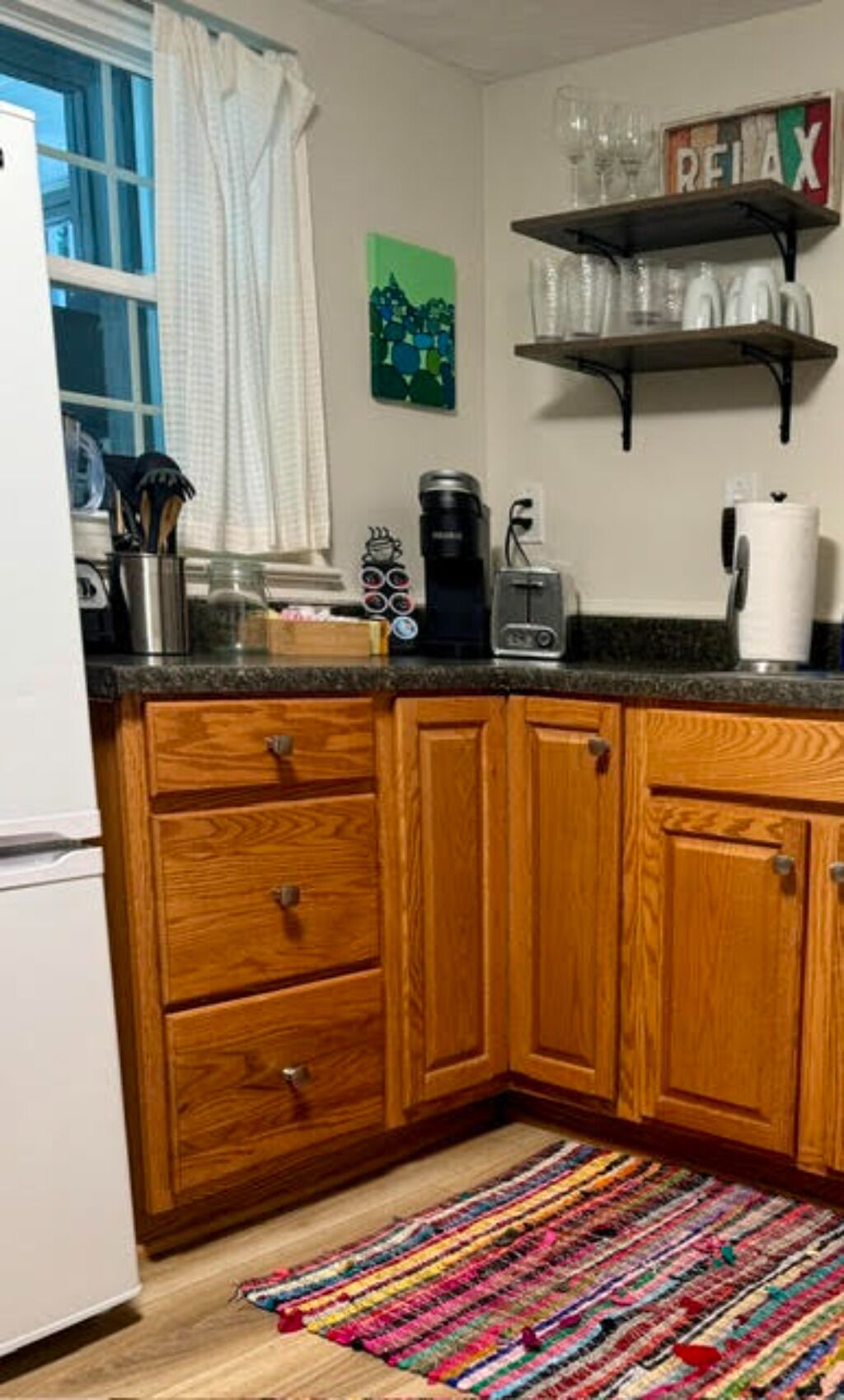 A kitchen with wooden cabinets, a coffee maker, a toaster, and a colorful rug on the floor.