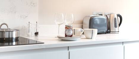Une cuisine moderne avec une bouilloire en acier inoxydable, un pot de confiture de fraises, une tasse blanche et un grille-pain.