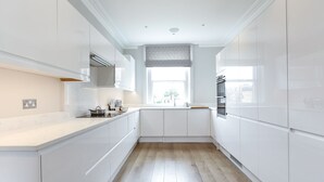 Eine moderne Küche mit weißen Schränken, Holzboden und einem Fenster mit einem gemusterten Rollo.