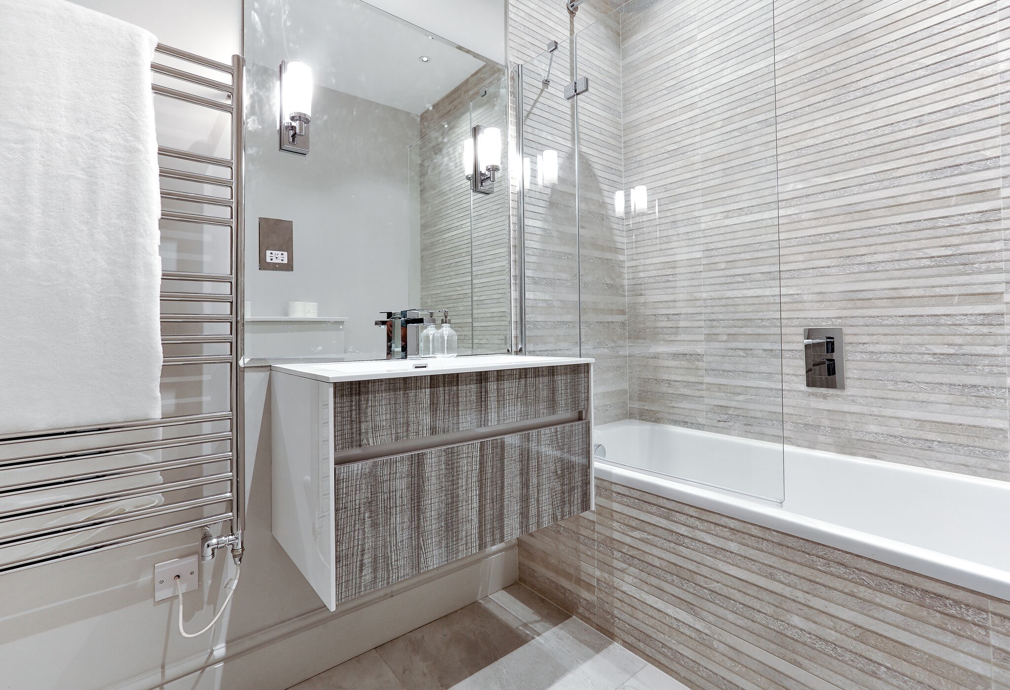 A modern bathroom with a glass shower enclosure, a white vanity with a textured backsplash, and a large bathtub.