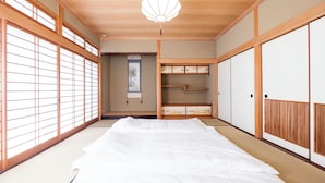 Une pièce de style japonais traditionnel, avec un sol recouvert de tatamis, un lit bas en bois, des portes coulissantes et un paravent shoji suspendu.