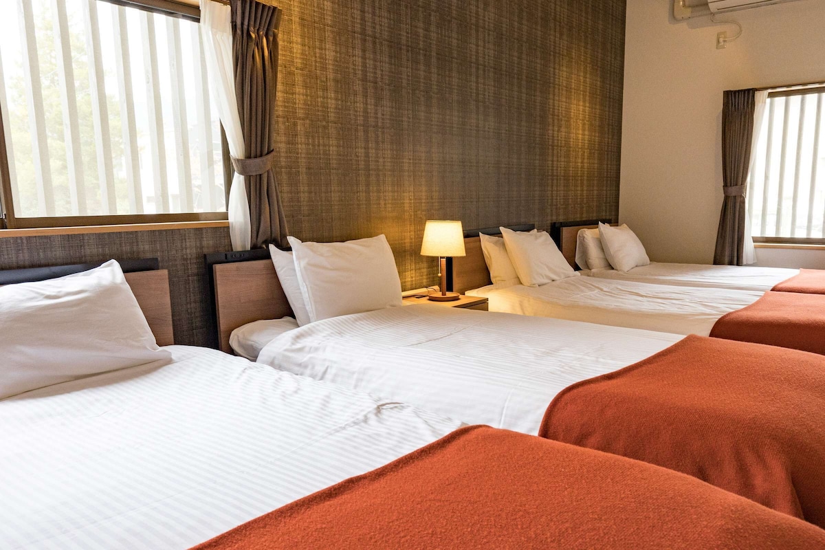 A hotel room with two beds, a nightstand with a lamp, and a window with curtains.