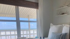 A bedroom with a view of the beach, a crib, a tray with bottles, and a bed with pillows. - Salt Air Cottage: Beachfront Charming & Luxe home! (Galveston)