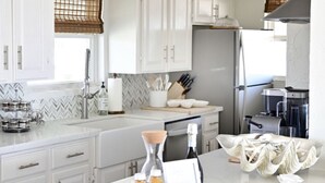 A modern kitchen with white cabinets, a marble countertop, and two pendant lights. - Salt Air Cottage: Beachfront Charming & Luxe home! (Galveston)