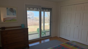 A bedroom with a wooden dresser, a colorful bedspread, a sliding glass door leading to a backyard, and a white closet.