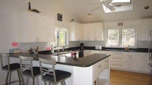 A modern kitchen with white cabinets, a central island with bar stools, a ceiling fan, and a window providing natural light.