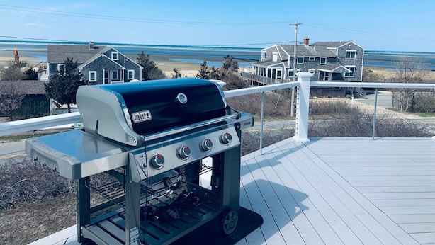A Weber gas grill on a wooden deck overlooking a beach and houses.