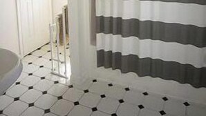 A bathroom with a white door, a shower curtain with horizontal stripes, and a tiled floor with a geometric pattern.