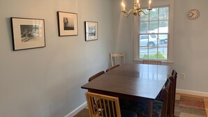 A dining area with a wooden table and chairs, framed pictures on the wall, a chandelier, and a window with a view of parked cars. - Less Than 1 Mile to Point of Rocks Beach (2186) (Brewster)